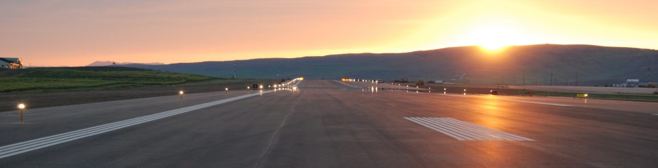 Yampa Valley Regional Airport runway at sunset with the sun peaking over a mountain in the background.