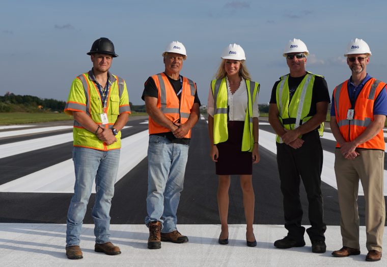 Beverly Regional Airport group photo on the runway. 5 people with hard hats and reflective vests on.